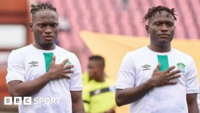 Identical twins Alhassan and Alusine Koroma, wearing white Sierra Leone shirts, both stand with their right hand over their heart during the national anthem